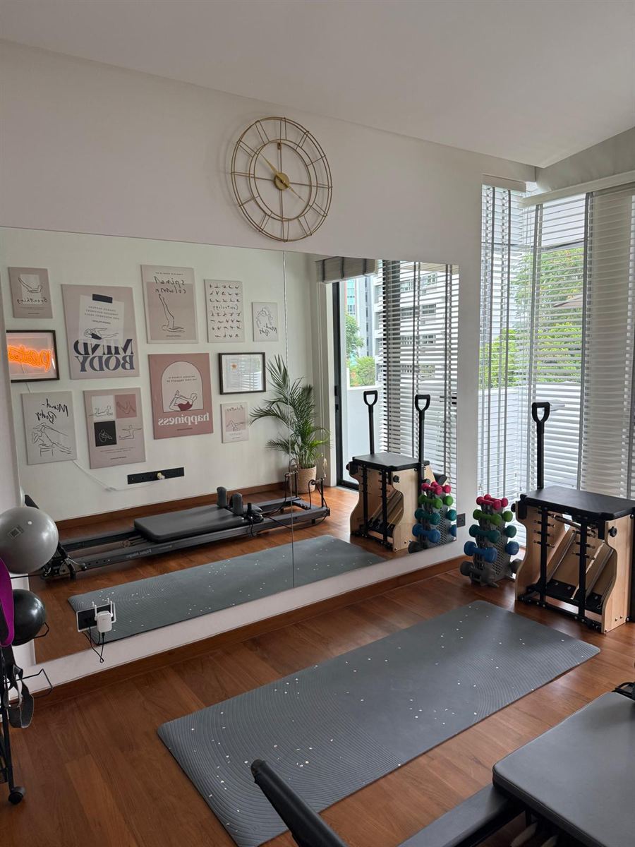 The studio: reformer, chairs, a mat and a mirrored wall of Pilates prints, with a gold clock above.