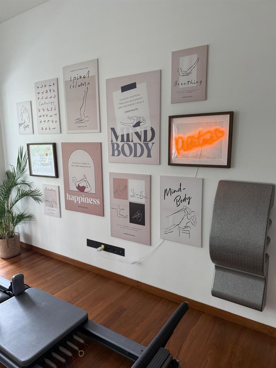 The studio's poster wall: Joseph Pilates quotes, line drawings and a neon Pilates sign, with a spine corrector beside it.